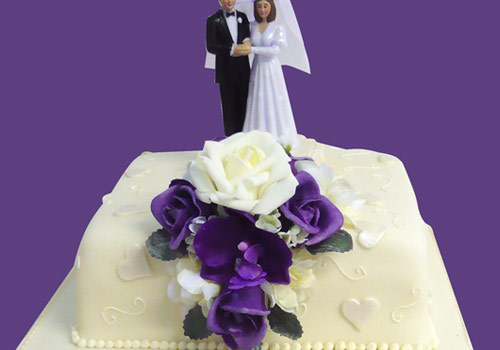 A purple themed Wedding Cake with bride and groom figures on top